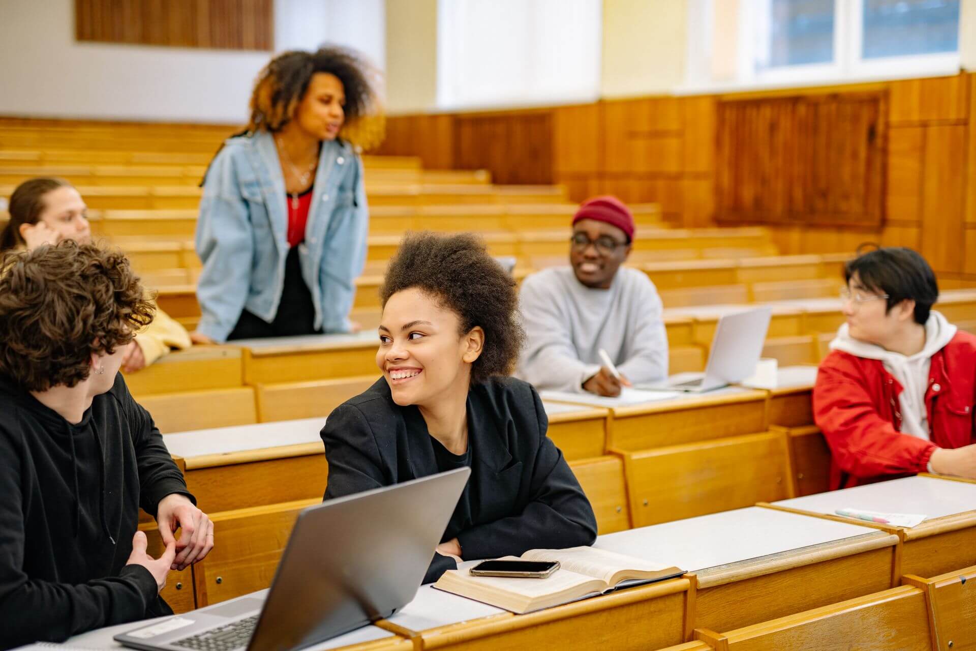 Un groupe d'etudiants qui echangent dans un amphitheatre, portables ouverts sur les pupitres.